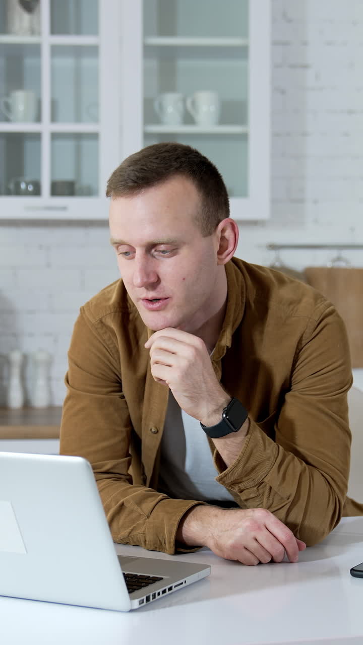 Student studying through the laptop in the kitchen. Young man working online in front of a wireless computer at home.Remote education. Vertical video