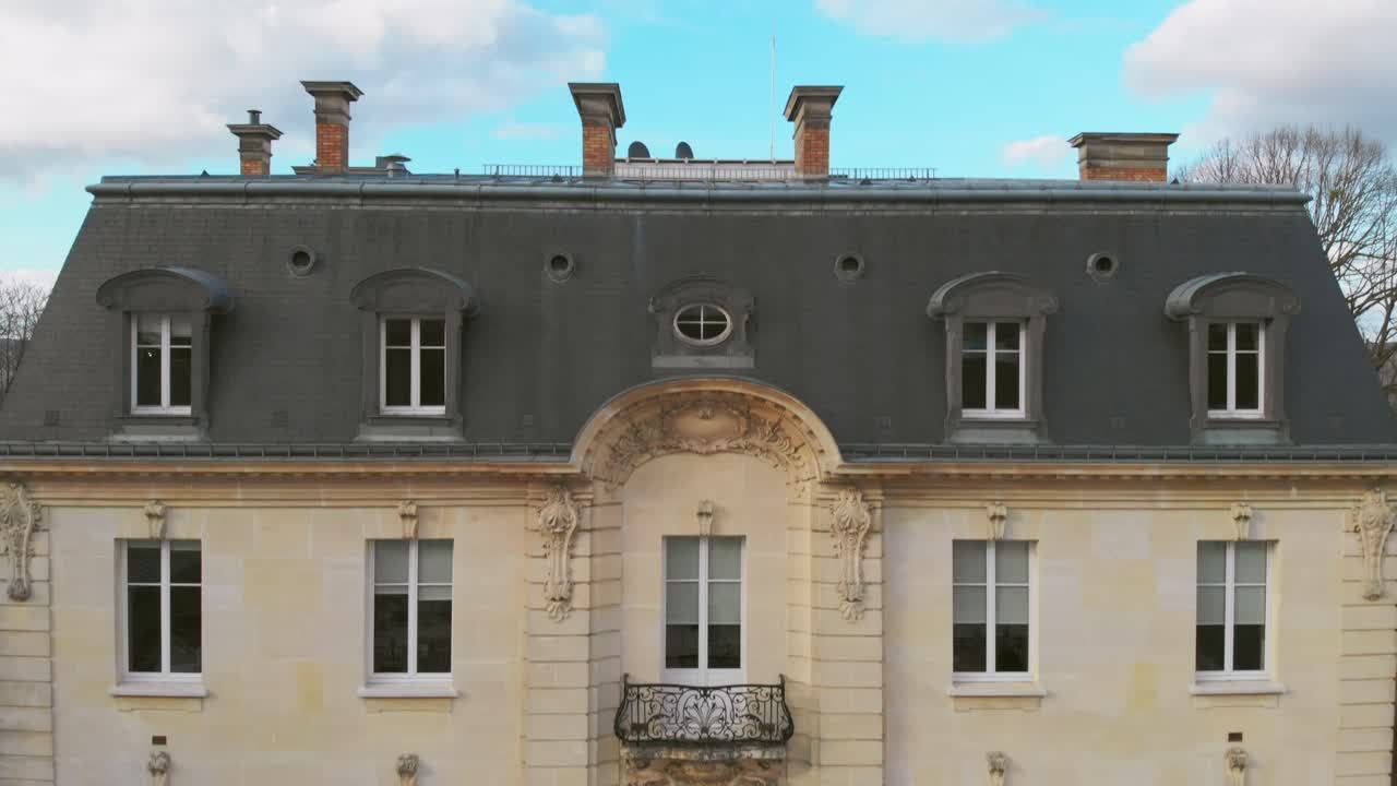 Aerial dolly up revealing a large historic building with a slate roof, set against the town of Champagne and rolling hills in the distance