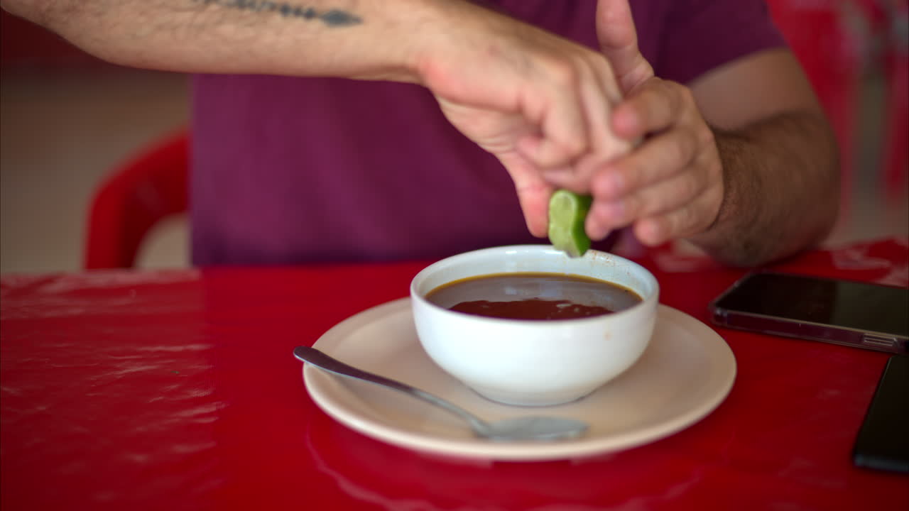 Slow motion of a latin man squeezing a lime into his broth stock soup in a mexican restaurant on a red table
