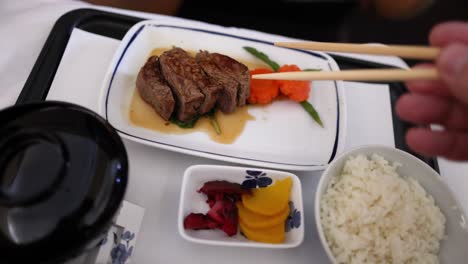 person eating steak, vegetables, and rice