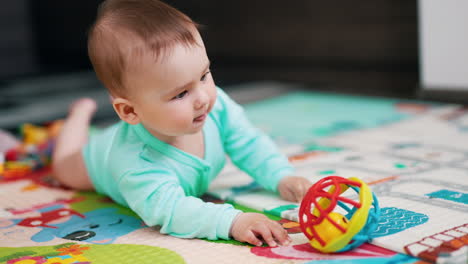 curious caucasian baby boy lying on the floor reaching a ball. sweet kid takes a toy and bangs it by the floor.