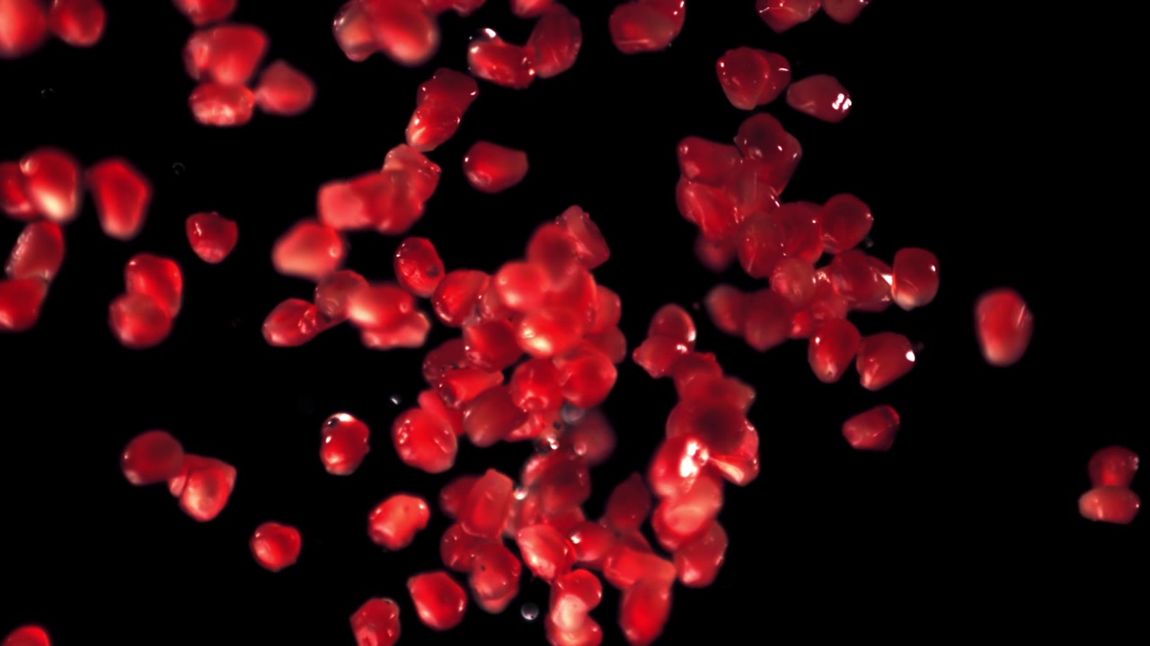 Red Pomegranate Seeds Falling in Slow Motion on Black Background