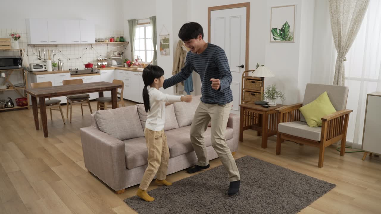 에너지 넘치는 아시아 아빠와 딸이 웃긴 움직임으로 춤을 춘 현대적인 거실에서 빛이 있는 집에서