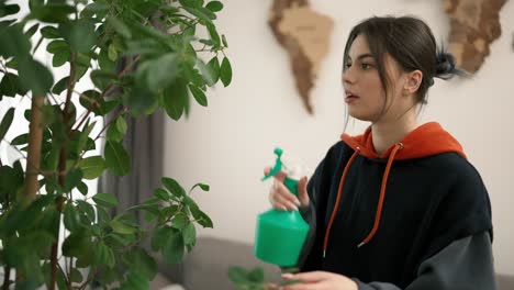 mujer rociando flores verdes en casa, cuidando las plantas del hogar
