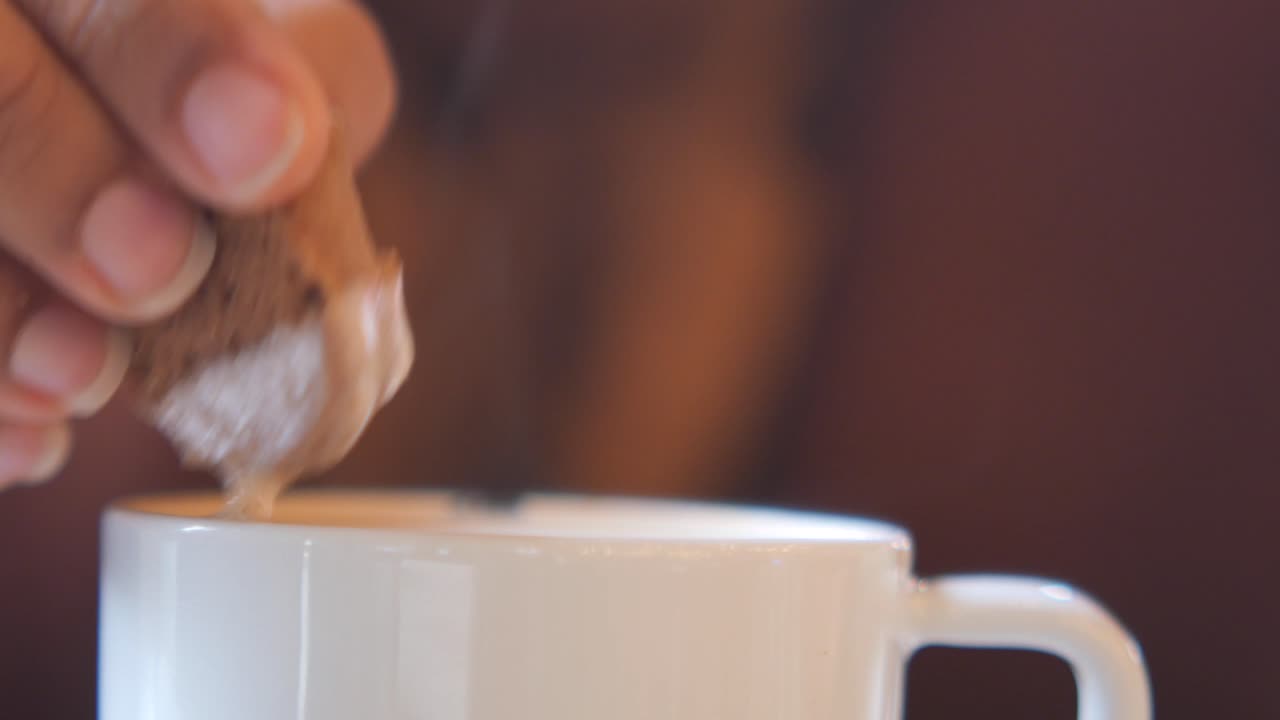 Close-up of a hand dipping a sugar cube in a cup of coffee