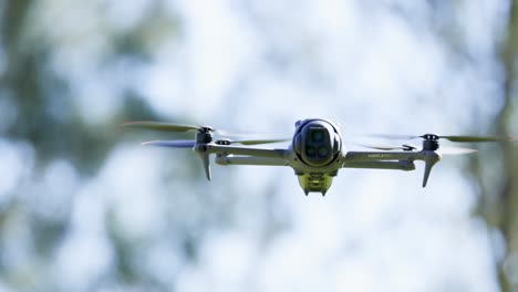 a drone hovers steadily against a backdrop of blurred trees, captured in slow motion with natural lighting