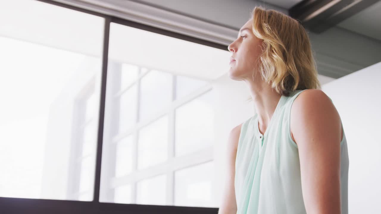 Professional businesswoman with hand on her chin looking out of a window from her modern office