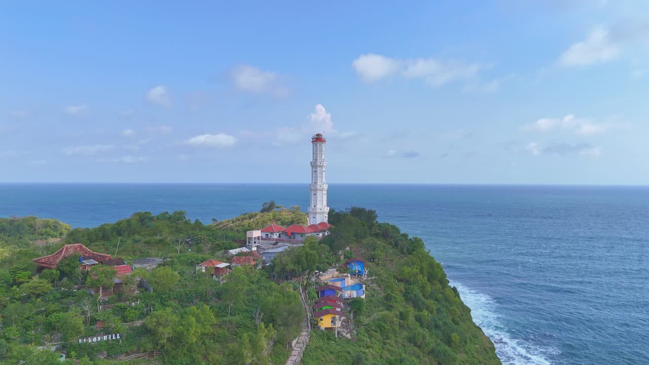 Scenic aerial coastal video showing a lighthouse on a hilltop, surrounded by lush vegetation and waves crashing below.Baron Beach Lighthouse, Indonesia