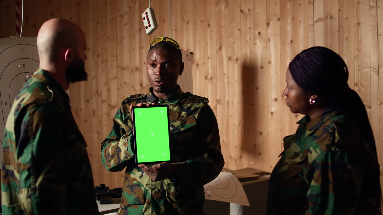Team of military units at shooting range watching video on green screen tablet