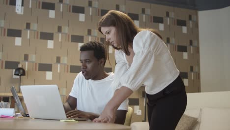 diverse coworkers sitting and standing at table with laptop