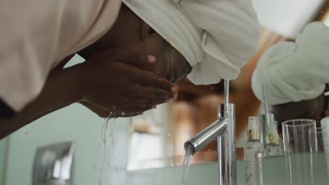 african american attractive woman washing off face mask in bathroom