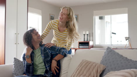 una pareja feliz y diversa abrazándose y sentada en el sofá en casa, en cámara lenta.
