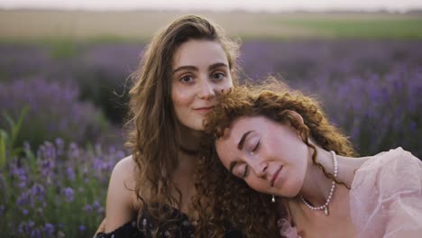 Portrait-of-two-curly-women-sitting-among-a-lavender-field,-embracing