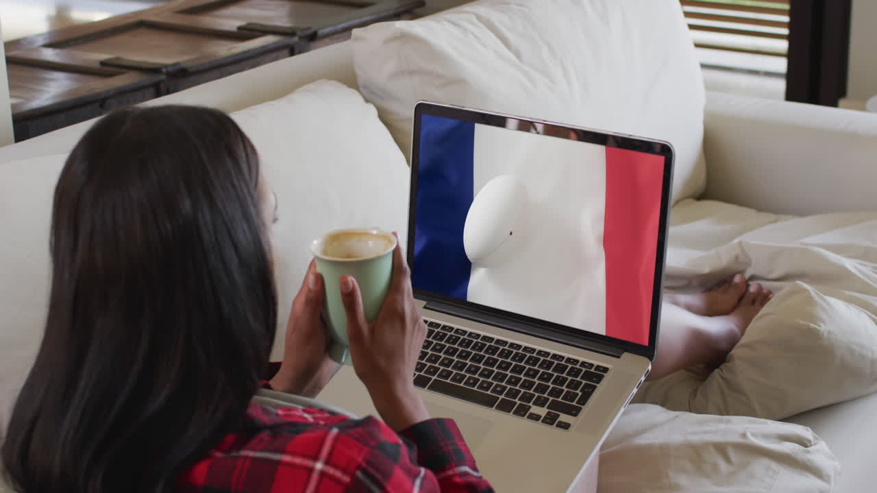 mujer biracial viendo una computadora portátil con una pelota de rugby con la bandera de francia en la pantalla