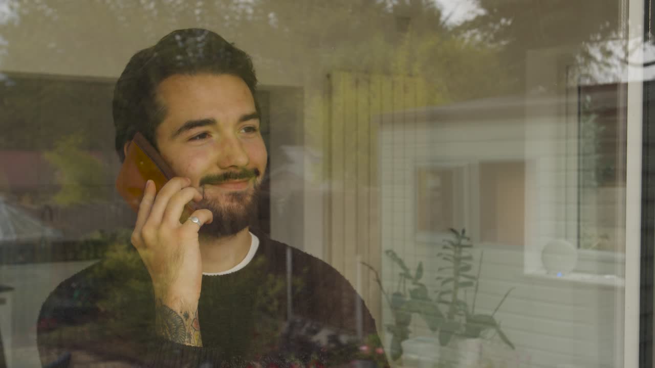 hombre mirando por la ventana mientras habla por un teléfono inteligente