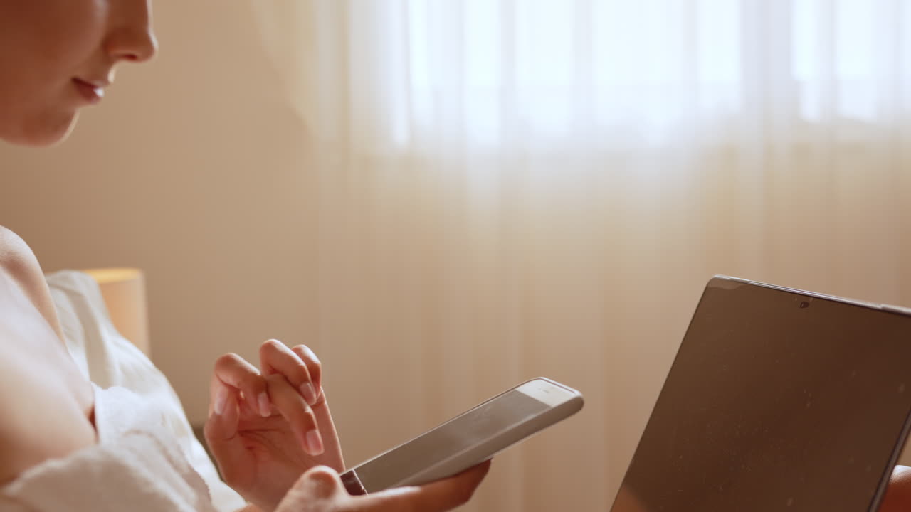 여자 는 전화 와 노트북 을 사용 하여 침대 에서 휴식 을 하고 있다