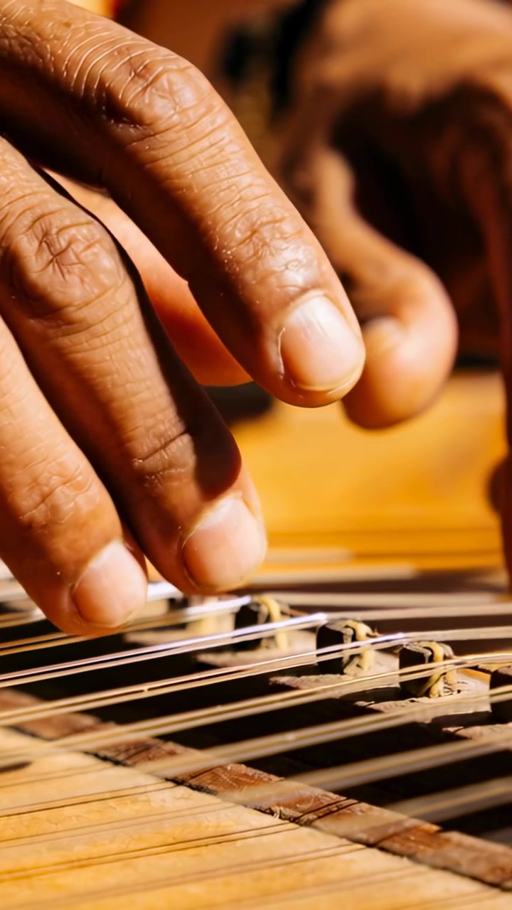 Video verticale: Mano di un uomo che pizzica le corde di una cetra nell'inquadratura, creando musica, con una manica scura.