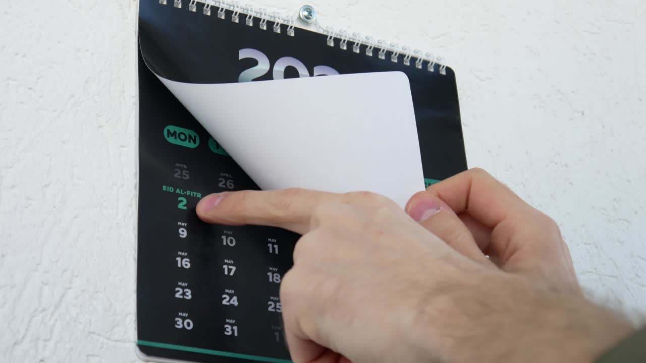 primer plano de manos masculinas girando el calendario de pared página abril 2022 y señalando un dedo a la fecha de eid al-fitr en el siguiente