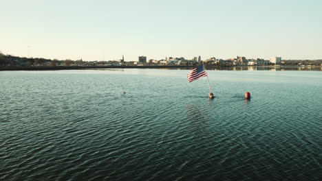 aerial of a flag flying in the wind attached to a buoy with portland maine skyline visible in the background