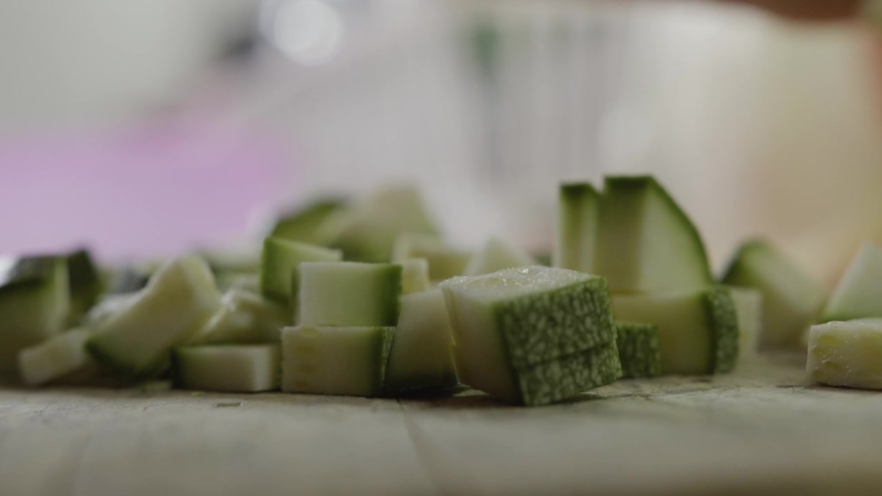 Primo piano di una mano che usa un coltello per raccogliere pezzi di zucchina tritati su un tagliere durante la preparazione di un pasto fresco in cucina