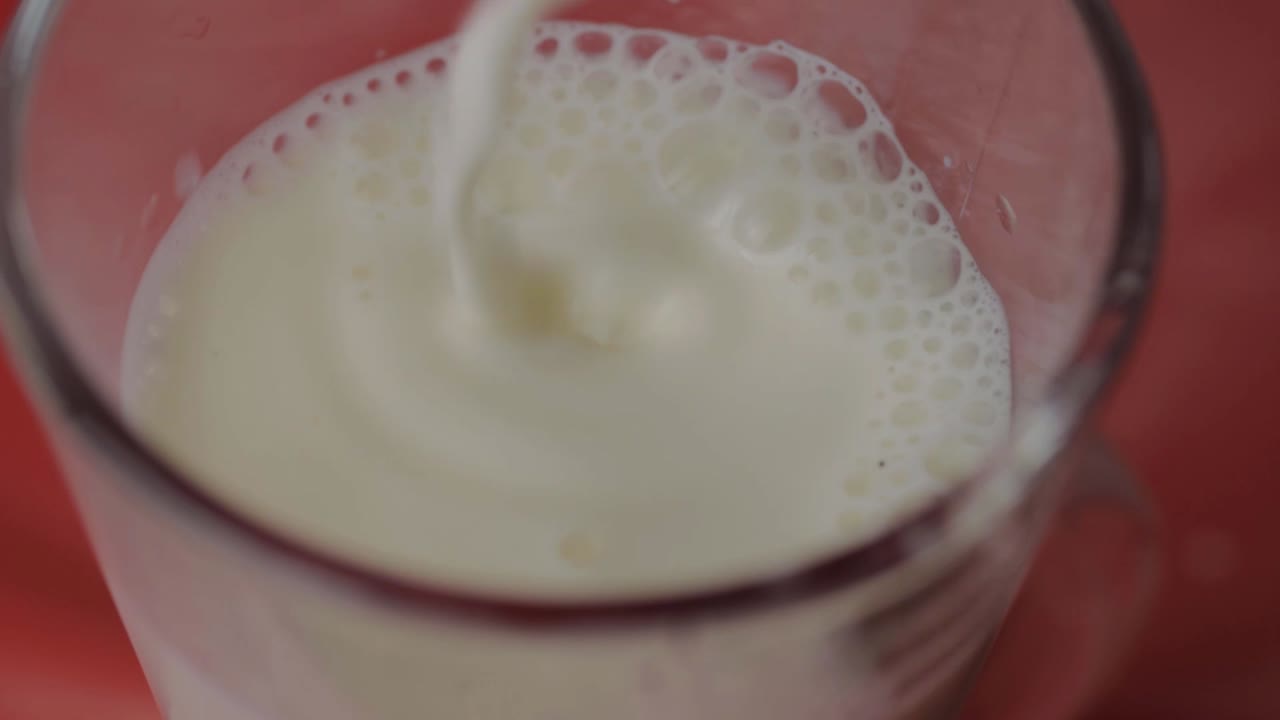 verter leche en un vaso sobre un fondo rojo.