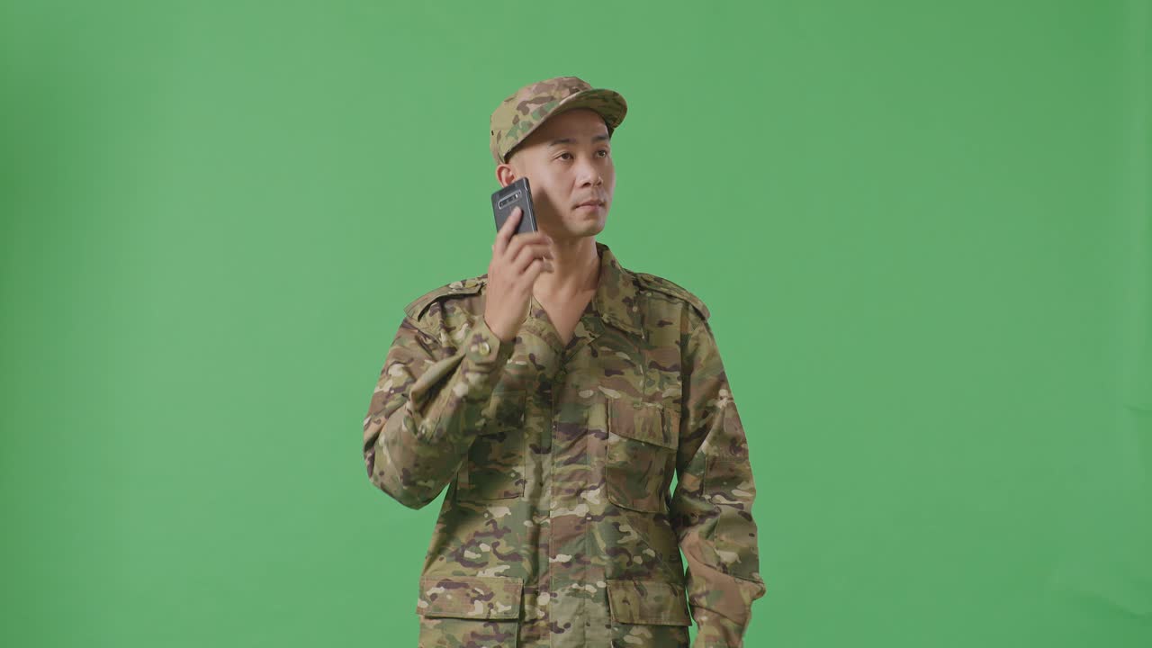 Asian Man Soldier Talking On Smartphone And Looking Around While Standing In The Green Screen Background Studio