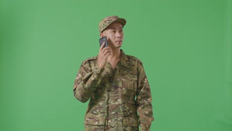 asian man soldier talking on smartphone and looking around while standing in the green screen background studio