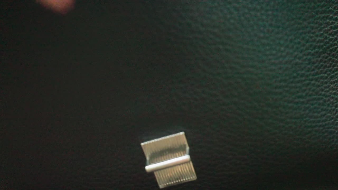 Close-up view of human hand opening and closing black leather bag with silver clasp, showing detailed texture of surface and metallic lock, capturing action in natural light for professional concept