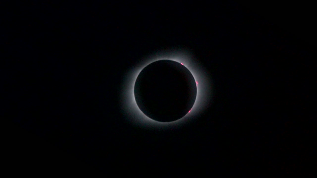 Rotating zoom-in on total solar eclipse showing pink prominences and solar corona