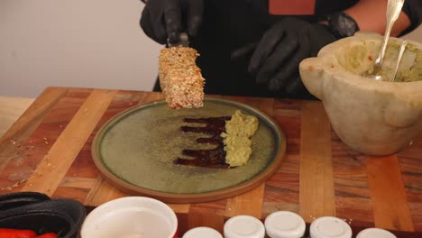 professional chef plating salmon tataki, carefully place the cooked fish fillet coated with white sesame seeds on top of smashed avocado salad on the ceramic plate in slow motion