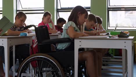 Niña-Con-Discapacidad-Física-Escribiendo-En-Su-Cuaderno-En-La-Clase.