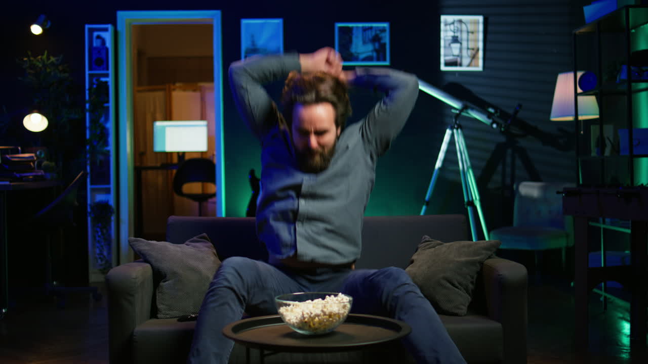 hombre molesto arrojando palomitas de maíz a la pantalla de la televisión en ira, viendo la transmisión deportiva