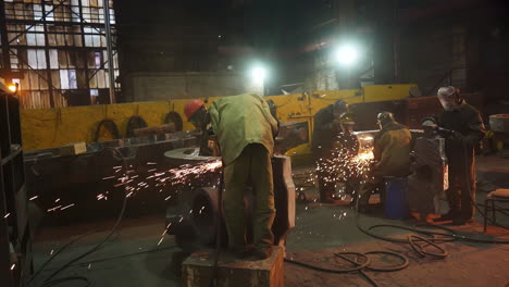 factory workers welding and grinding metal parts at night