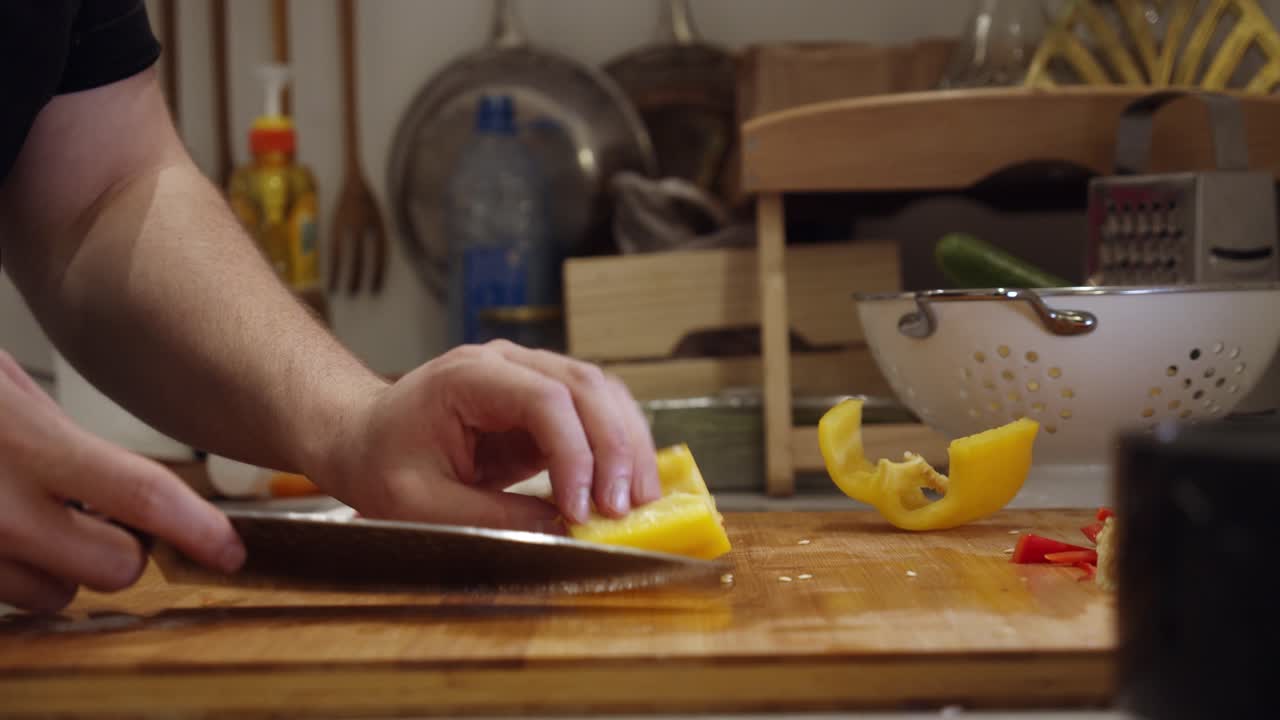 el chef corta la mitad de la pimienta de color amarillo grande con un cuchillo de acero en una tabla cortada de madera en una mesa de cocina