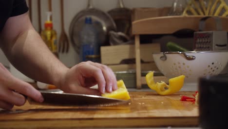 chef cuts in half big yellow color pepper with steel knife on wooden cut board on a kitchen table