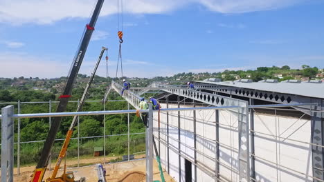 Construction-Workers-Work-at-Height-to-Attach-Steel-Beam-to-Structure,-Drone-POI