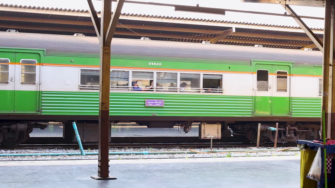 Static platform view of passing commuter train, cleaning cart and bench under bright daylight