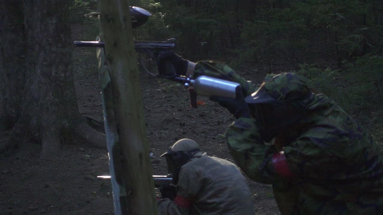 페인트볼 선수가 숲의 전투장에서 컬러 스플래시로 총을  ⁇ 고 있습니다.