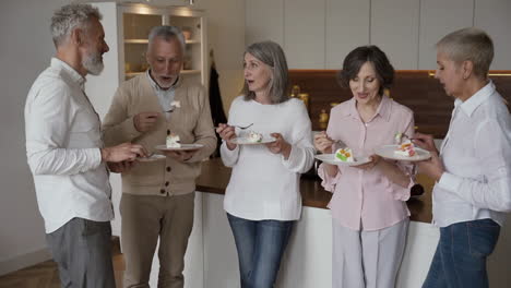 group of cheerful senior friends chatting and eating a delicious dessert, standing in a modern style kitchen 4