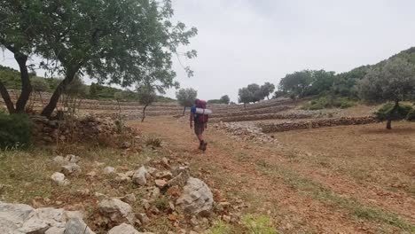 Un-Excursionista-Masculino-Solitario-Caminando-Por-Campos-Vacíos-En-Una-Pequeña-Pendiente-Al-Estilo-Licio-Turco-Durante-Un-Verano-Caluroso