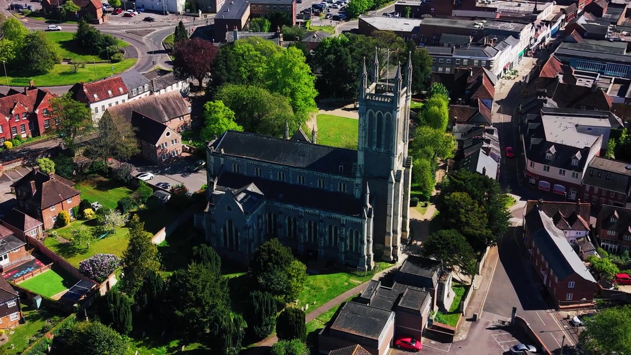 Letecké záběry z dronu kroužící kolem kostela svaté Marie v Andoveru, ukazující historickou kostelní věž, kamennou architekturu, kostelní areál, okolní ulice, střechy, domy, stromy a zelené plochy.