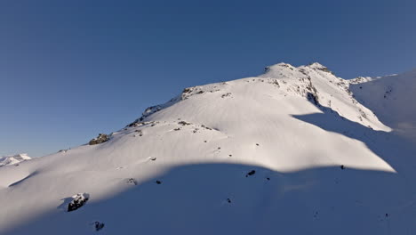 aerial drone shot of a snowboarder carving fresh powder down steep verbier slopes on a pristine bluebird day, white spray and dramatic alpine peaks in the background