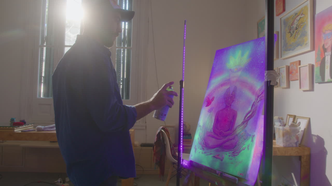 Male Artist Spraying UV Paint of Canvas Painting in Art Studio