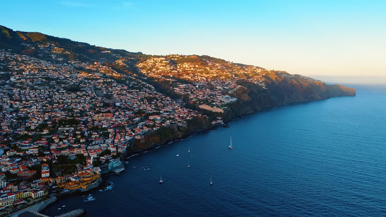 Densely populated slopes of the mountains on the coast of the North Atlantic Ocean. Some yacht sail at the shore of the Madeira Islands, Portugal. Aerial view.