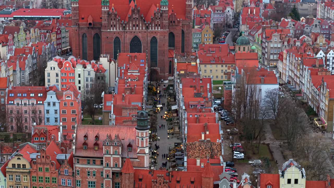 Aerial of St Mary Gate cobbled street shops on Mariacka revealing ancient brick gotic St Marys catholic church in old town of Gdansk surrounded with buildings in the evening, Europe