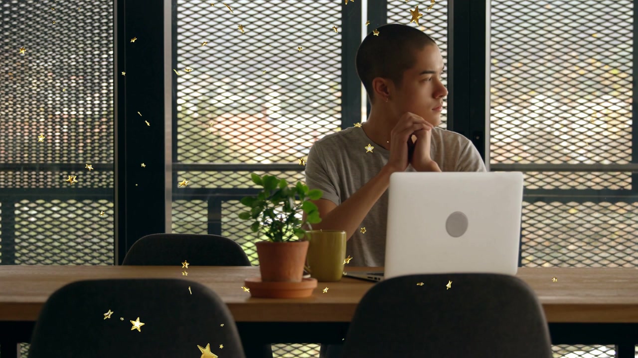 Man starting laptop work, clasping chin, glancing at mesh window while gold stars drifting in front