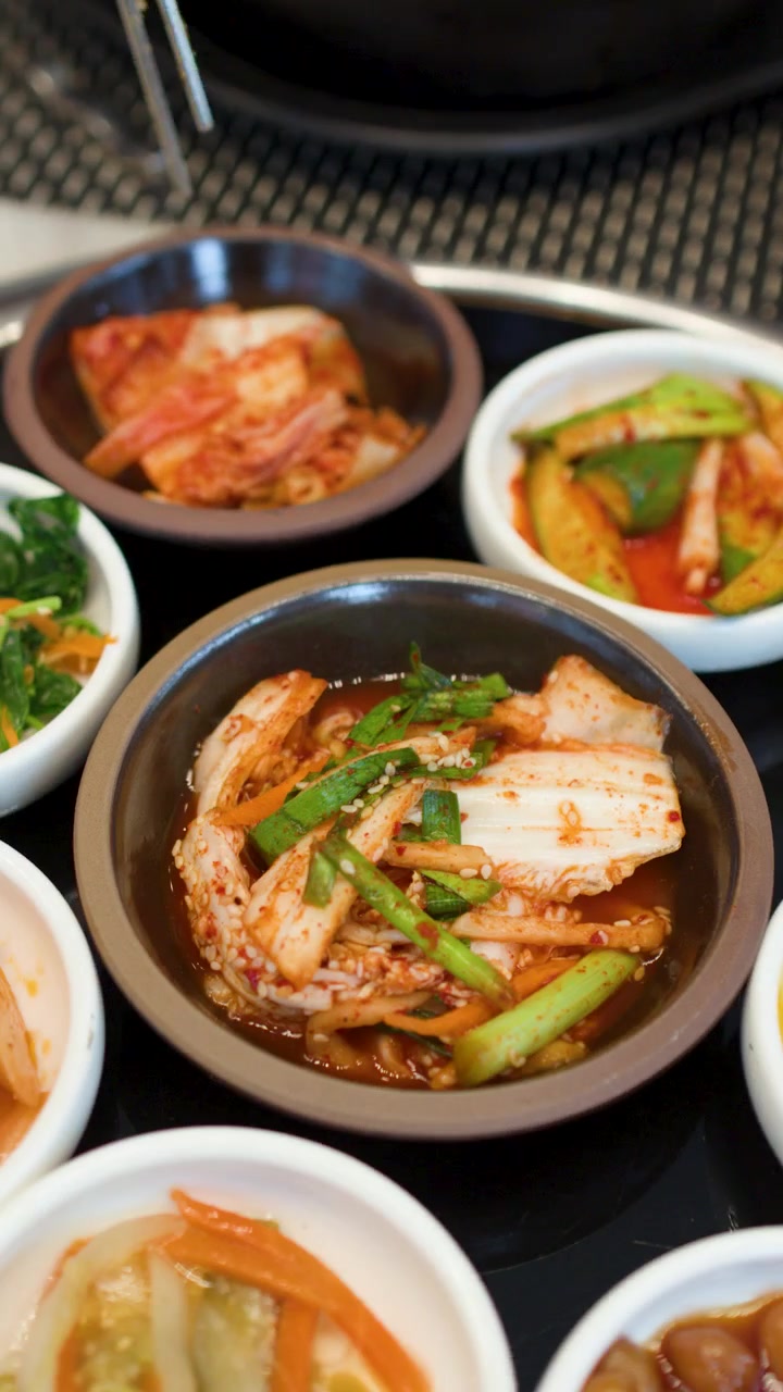 Foto close-up mencampur bibimbap dalam mangkuk dolsot diikuti dengan berbagai lauk kimchi.