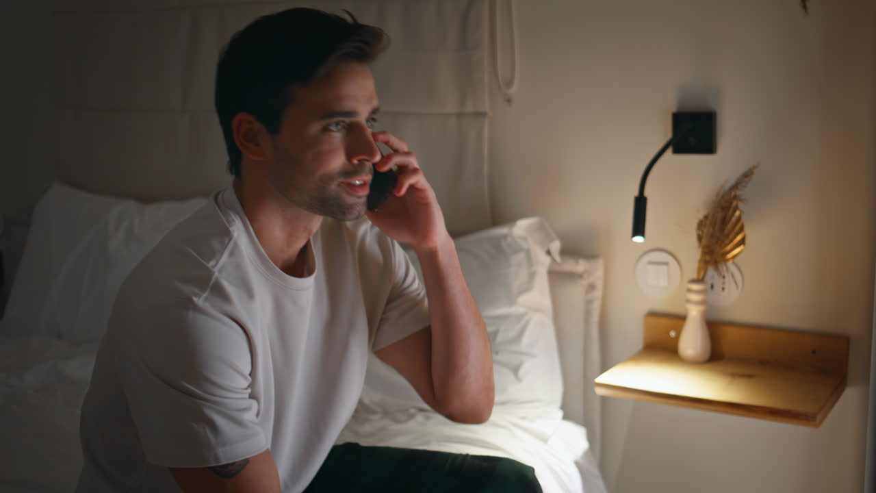 Guy talking cellphone bed at tranquil night home atmosphere closeup. Man calling