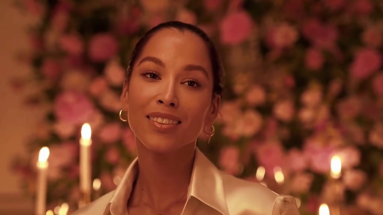 Donna elegante che sorride davanti a uno sfondo floreale con candele.