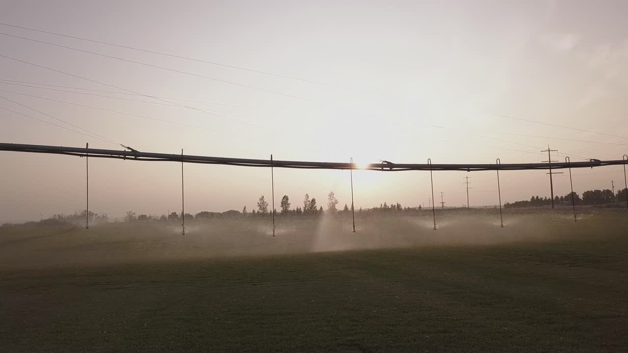 Aerial dolly shot of pivot irrigation system watering crop near sunset